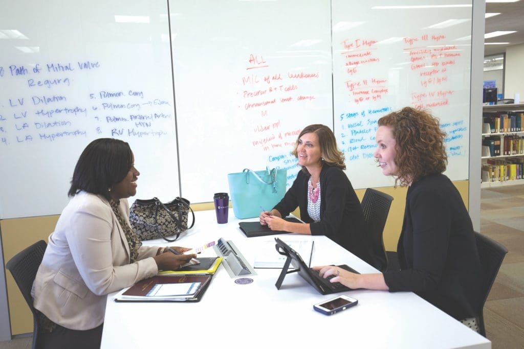Three adult students talking at a table inside the Learning Commons