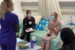A social work student watches (right) as two nursing students ask the "patient" questions about her health.