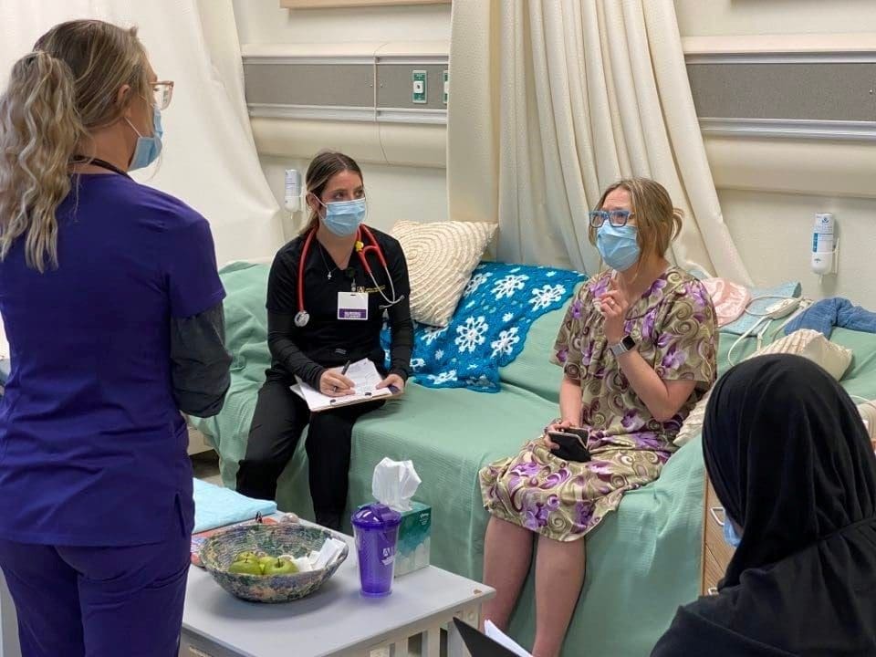 A social work student watches (right) as two nursing students ask the "patient" questions about her health.