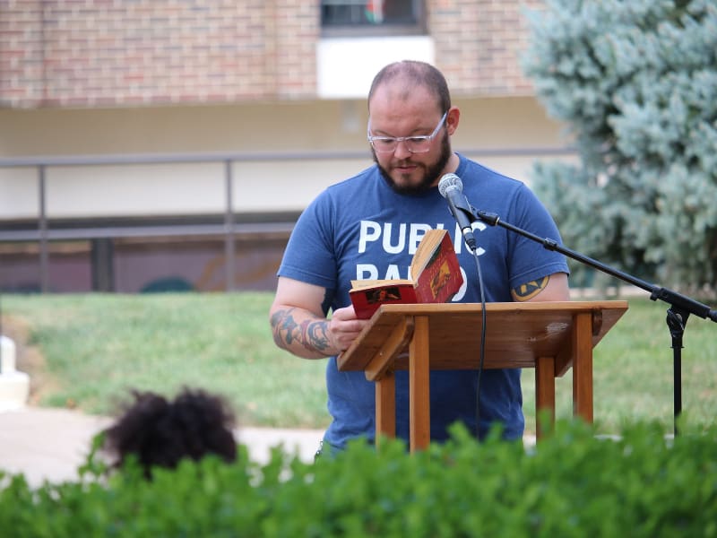 Young man reading from book at outdoor lecturn