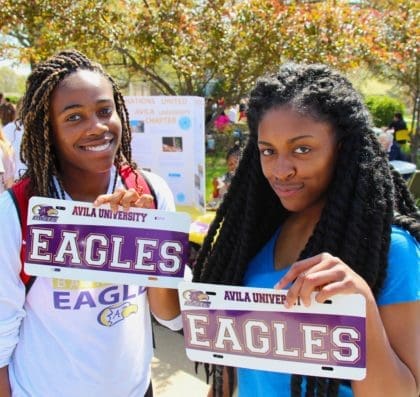 Two students proudly holding up the personalized license plates they created at a campus carnival. Both license plates say "Eagles"
