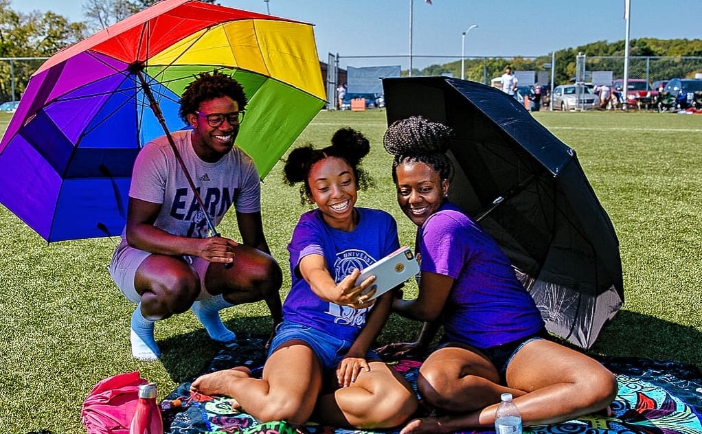 Three students taking a selfie on the football field sidelines